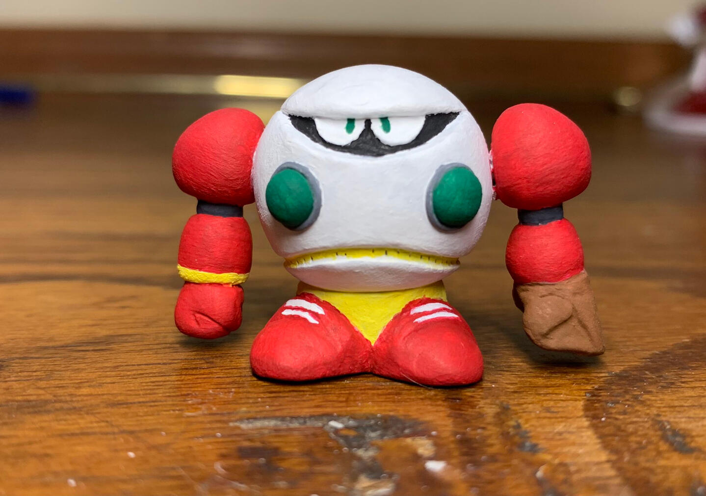 a chibi styled clay figure of strike man it sits on a wooden desk